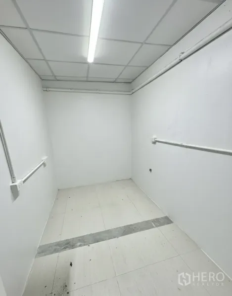 พื้นที่ขายปลีก ให้เช่า - ห้องเก็บของด้านหลังขนาดกะทัดรัด ผนังสีขาว ไฟเพดาน และท่อยูทิลิตี้