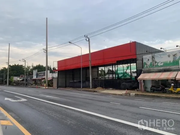 คลังสินค้า ให้เช่าในBueng Kum, Bangkok - มุมเอียงเห็นโกดังสีแดงติดถนนหลายเลน มีเสาไฟฟ้าและร้านค้าใกล้เคียง