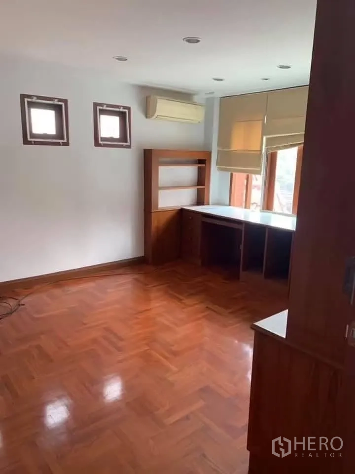 Townhouse for rent in Watthana, Bangkok - Corner room with wooden floors, air conditioner, and long built-in desk and shelves.