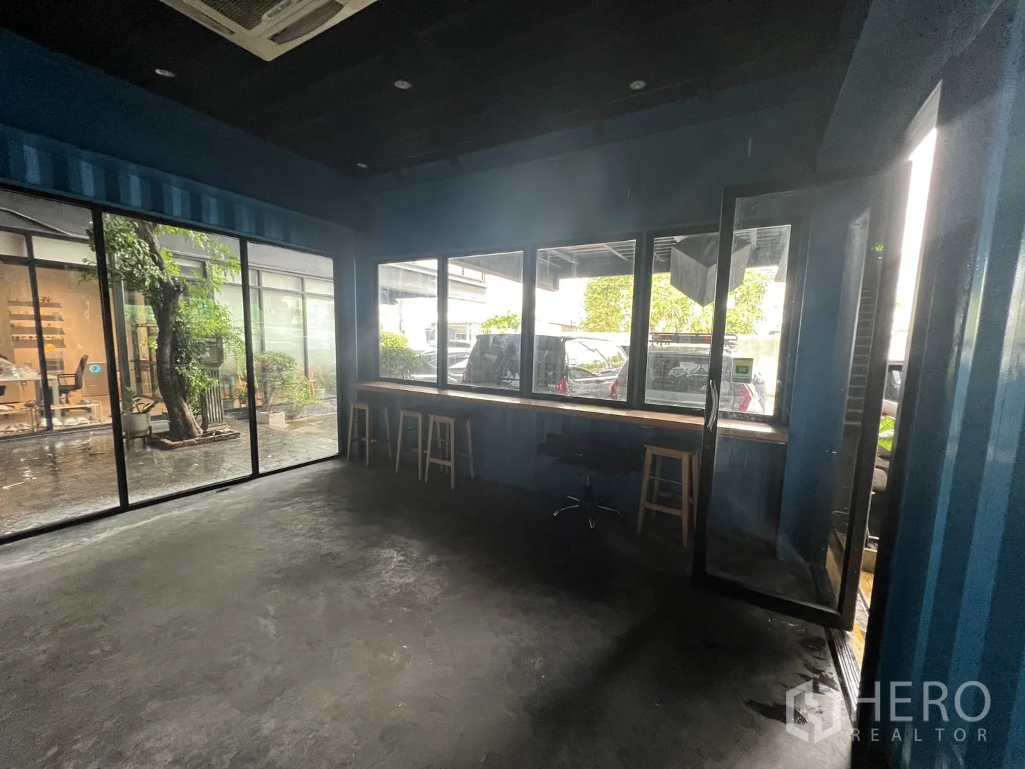 พื้นที่ขายปลีก ให้เช่า - มุมกระจกเต็มสูง พร้อมเคาน์เตอร์ริมหน้าต่างและสตูล หันสู่ลานมีต้นไม้