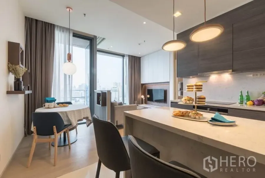 Condominium for rent in Watthana, Bangkok - Modern open-plan kitchen with island, pendant lights, dining table, and floor-to-ceiling windows overlooking the Bangkok skyline.