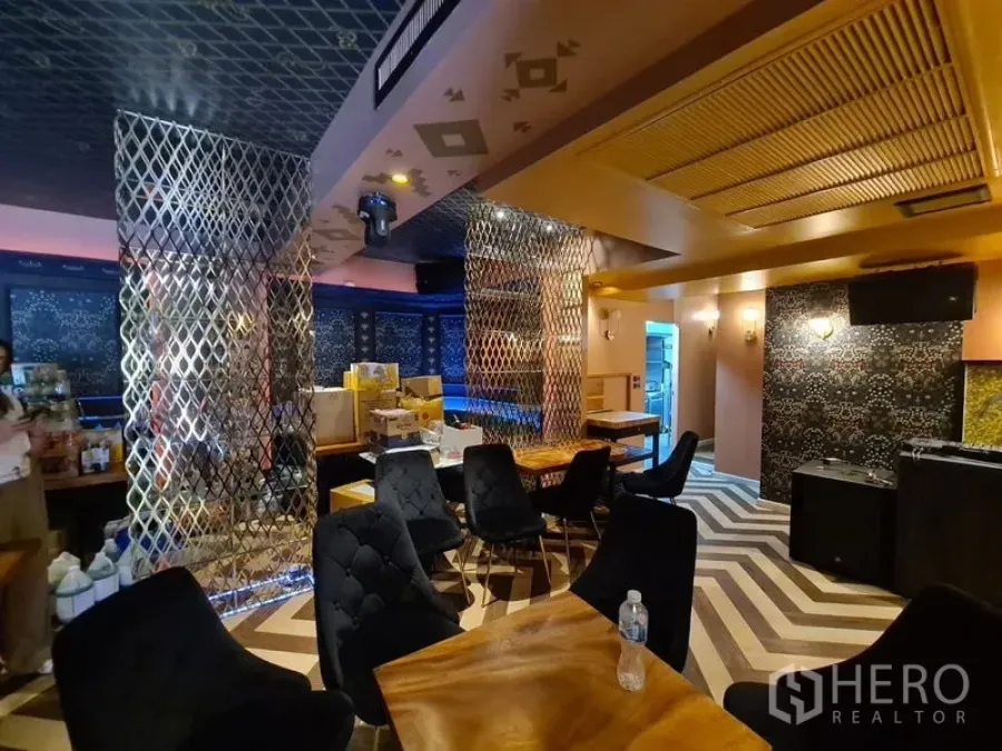 零售空间 出租在Bang Rak, Bangkok - 休闲区铺人字拼地板，软包椅、木桌与金属隔断分区。