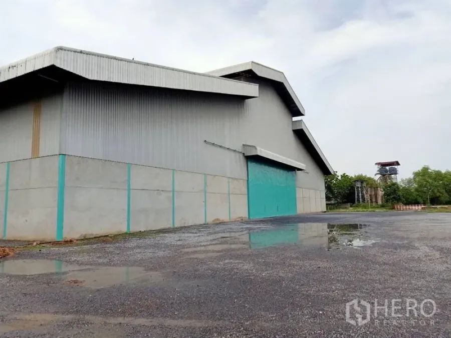 Factory for rent in Chaloem Phra Kiat, Saraburi - Side view of the factory showing wide loading apron, drainage, and greenery around the site.