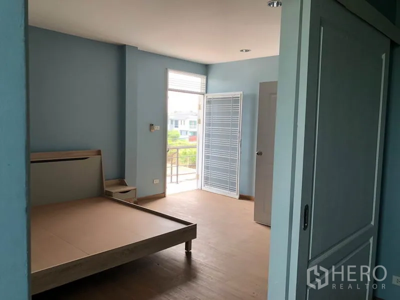 独立式住宅 出售在Bang Khen, Bangkok - 宽敞卧室，带床架、推拉门、木纹地面和小阳台出入口。