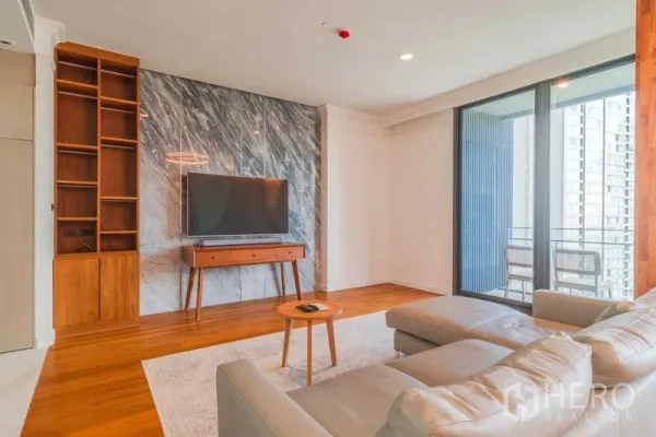 Condominium for rent or sale - Bright living room with marble feature wall, mounted TV, wood floors, and sliding doors to a balcony with city view.