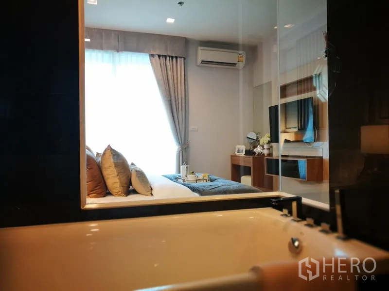 公寓 出租在Sathon, Bangkok - 浴室设浸泡浴缸，可通过玻璃隔断望向带电视的卧室。