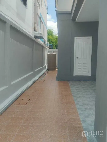 บ้าน ขายในPhra Khanong, Bangkok - ทางเดินข้างบ้านปูกระเบื้อง พร้อมกำแพงสูงและประตูห้องเอนกประสงค์สีขาว
