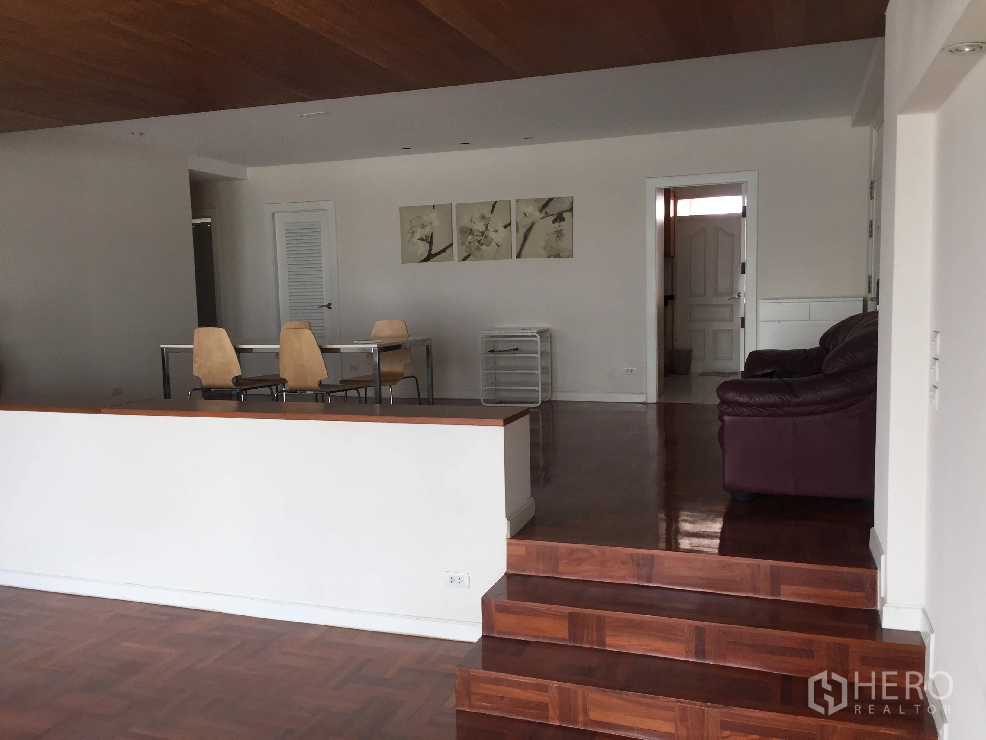 Condominium for rent in Sathon, Bangkok - Split-level open-plan area with dining table, leather sofa, wood floors and white walls.