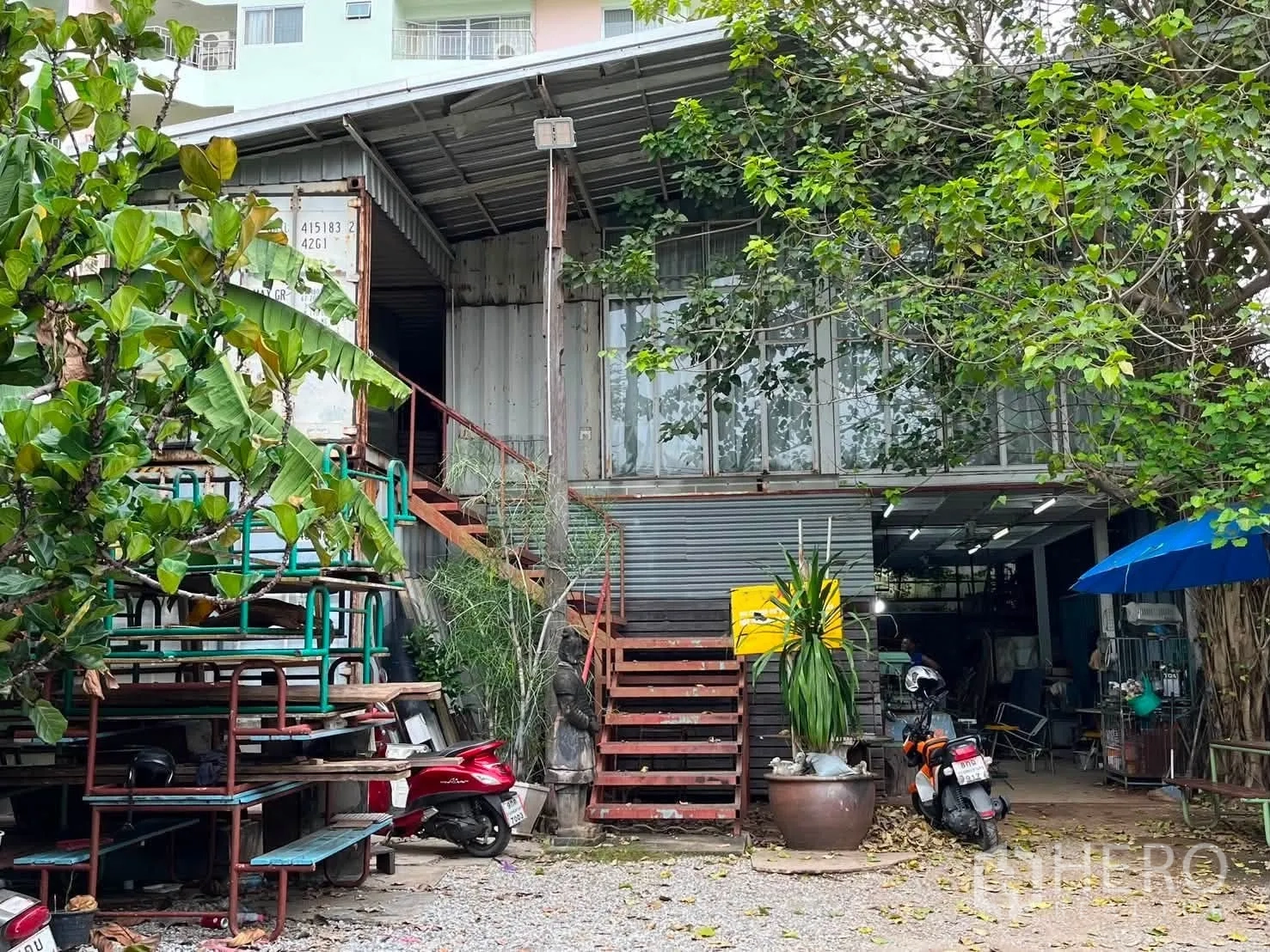 โกดัง for rent in Watthana, Bangkok - ด้านหน้าโกดังสองชั้นโครงเหล็กพร้อมบันไดนอกอาคาร ลานกรวด และต้นไม้ใหญ่