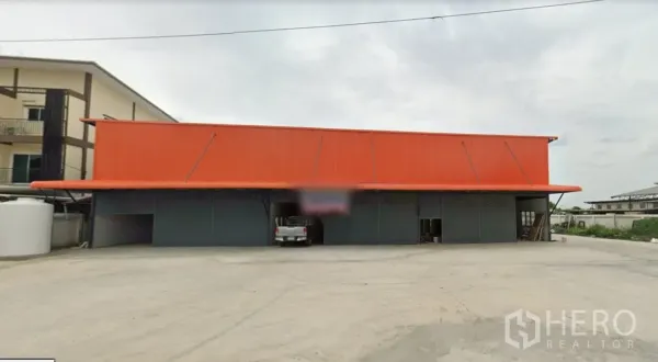 货栈 出租在Lam Luk Ka, Pathum Thani - 橙色金属屋顶的仓库外观，临街多扇卷帘门，前方大面积混凝土场地。