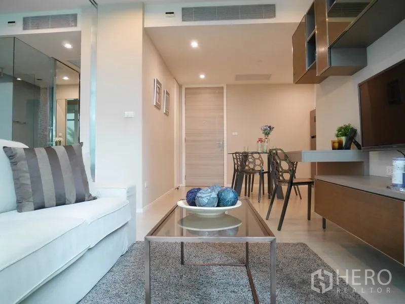 Condominium for rent or sale in Watthana, Bangkok - Bright living and dining area with sofa, glass coffee table, built-in cabinetry and recessed lighting.
