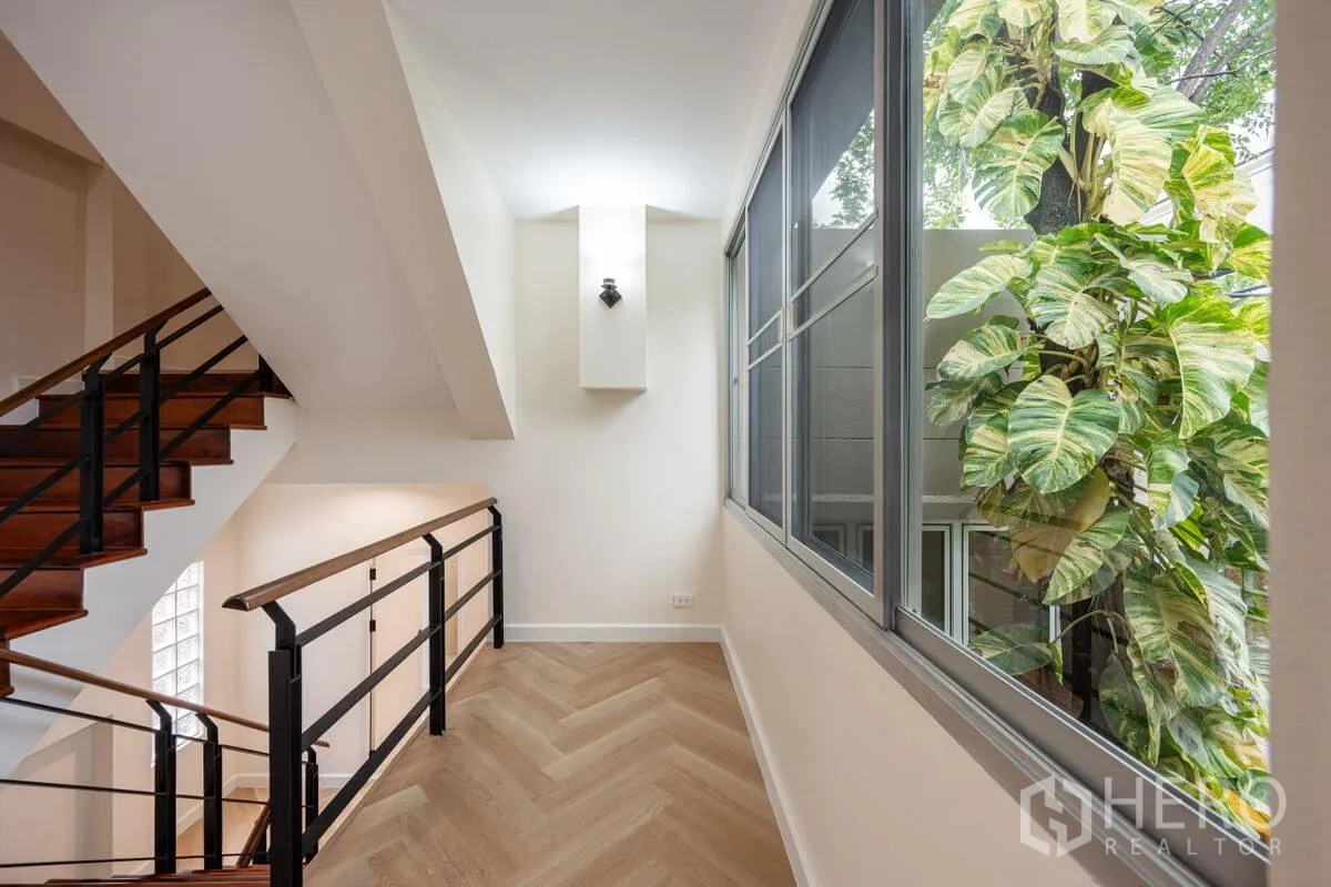 Detached House for rent or sale in Chatuchak, Bangkok - Upper landing with herringbone floor, metal railing, and large window beside lush greenery.