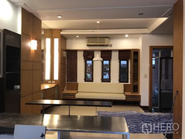 Townhouse for rent or sale in Watthana, Bangkok - Open-plan living and dining area with built-in seating, wood accents and a central pendant light.