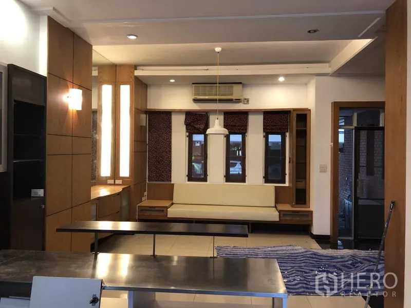 Townhouse for rent or sale in Watthana, Bangkok - Open-plan living and dining area with built-in seating, wood accents and a central pendant light.