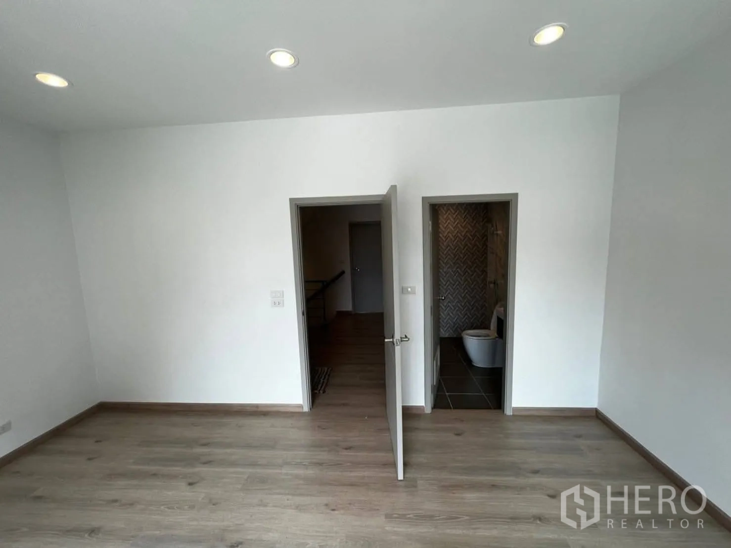 Townhouse for rent in Bang Khen, Bangkok - Front bedroom with large window, recessed lights, and laminate floors.