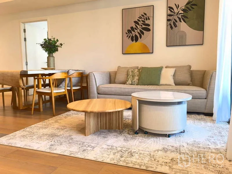 อพาร์ทเมนท์ ให้เช่า - มุมห้องนั่งเล่นโชว์โซฟาโทนกลาง โต๊ะกาแฟทรงกลม และชุดโต๊ะอาหาร