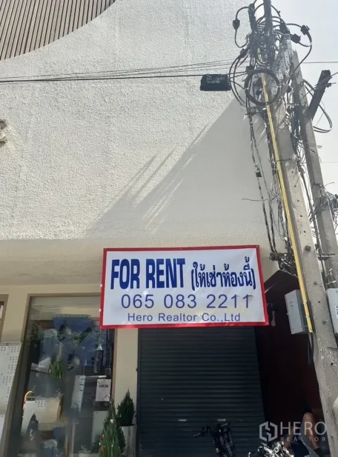 零售空间 出租在Watthana, Bangkok - 一层店面外观，挂有出租招牌，卷闸门、玻璃橱窗与街边电线。