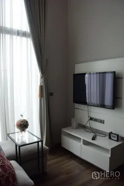 Condominium for rent in Watthana, Bangkok - Wall-mounted TV and white media console next to a tall window with sheer drapes.