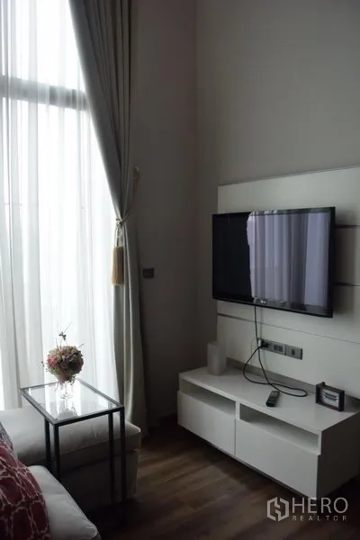 Condominium for rent in Watthana, Bangkok - Wall-mounted TV and white media console next to a tall window with sheer drapes.