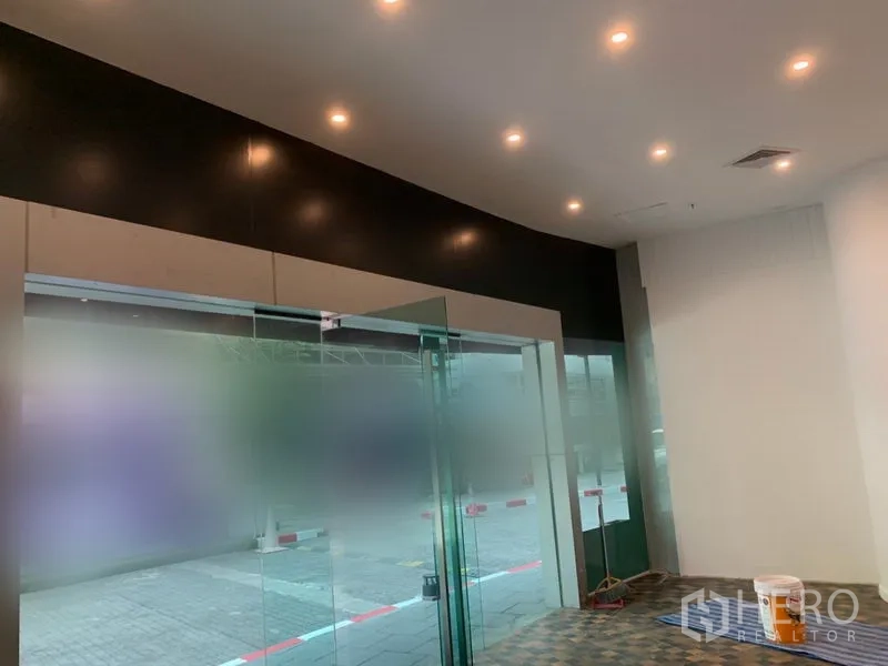 零售空间 出租在Khlong Toei, Bangkok - 室内视角，玻璃入口、嵌入式筒灯与瓷砖地面。