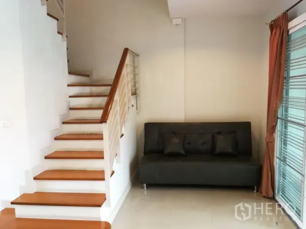 Townhouse for rent in Phasi Charoen, Bangkok - Staircase with wooden steps next to a sofa and sliding glass door.