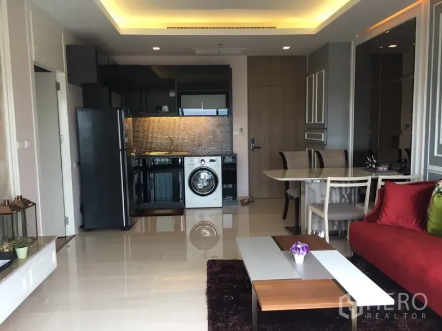 Condominium for rent or sale in Watthana, Bangkok - Open-plan living room with red sofa, dining table, and a modern kitchenette with built-in washer.