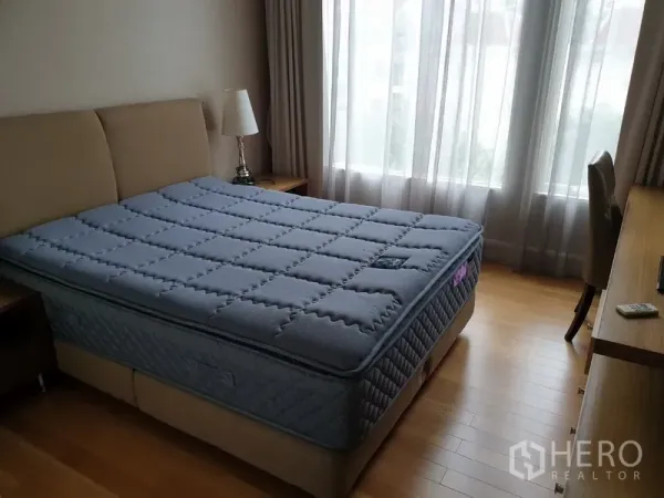 Condominium for rent in Watthana, Bangkok - Cozy bedroom with queen bed, work desk, large window with sheer curtains and warm wood flooring.