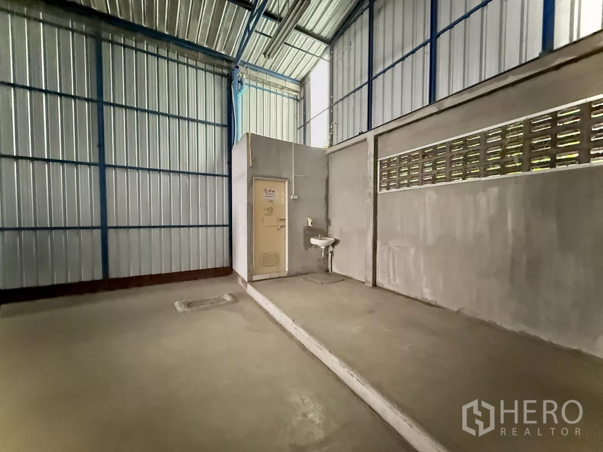 Warehouse for rent in Bueng Kum, Bangkok - Warehouse corner with built-in restroom, sink and ventilation blocks under a metal roof.