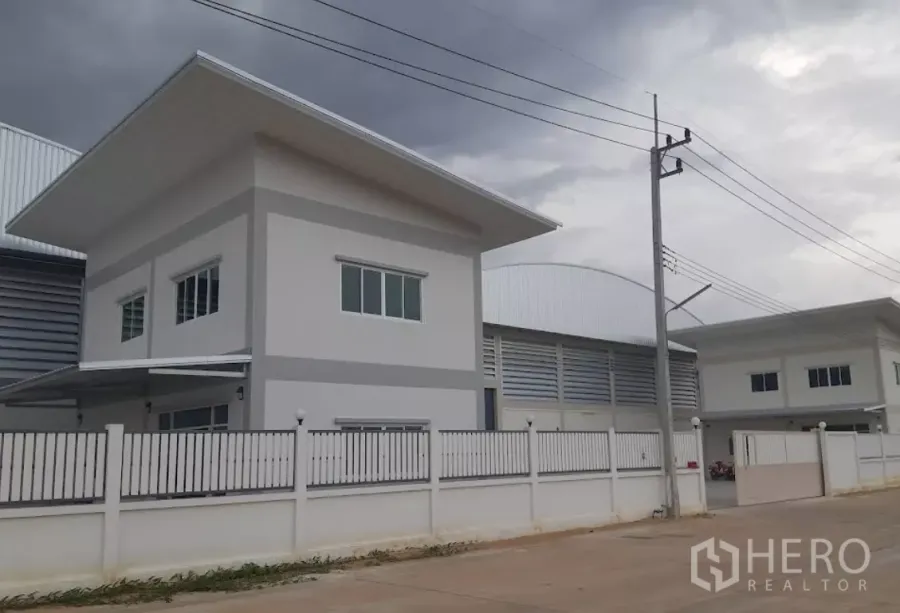 工厂 出租在Nakhon Pathom - 三攀工业园内带围栏的现代厂房与两层办公楼，临宽阔道路，阴天景色。