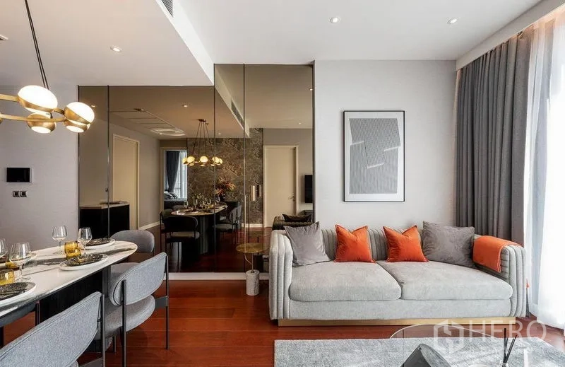 公寓 出租在Watthana, Bangkok - 客厅设镜面墙与灰色沙发橙色抱枕，可见餐区景致。