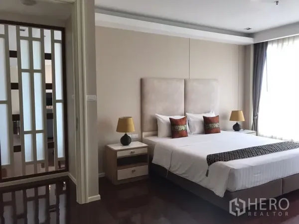 房间 出租在Khlong Toei, Bangkok - 主卧配特大床与床头柜，柔和灯光，旁有装饰隔断。