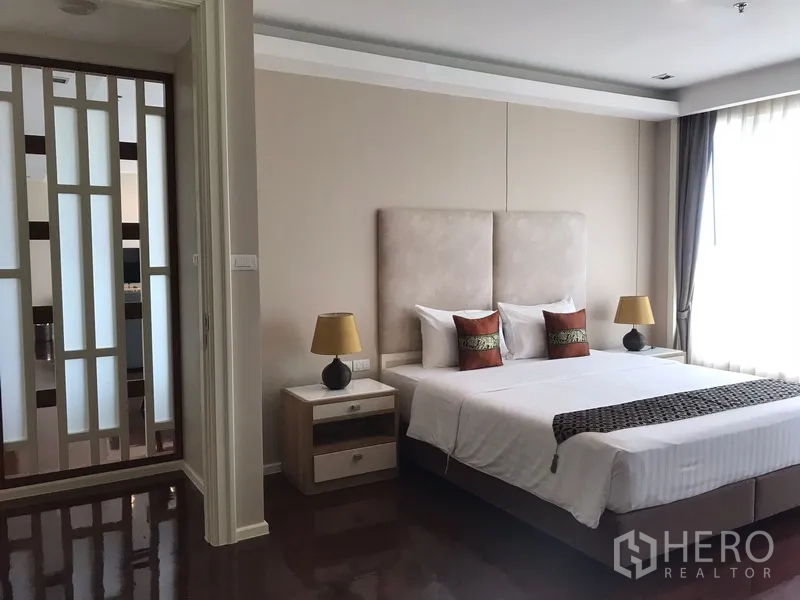 房间 出租在Khlong Toei, Bangkok - 主卧配特大床与床头柜，柔和灯光，旁有装饰隔断。