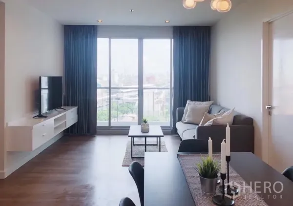 Condominium for rent in Bang Rak, Bangkok - Living room facing wide balcony doors with TV console, sofa and city outlook.