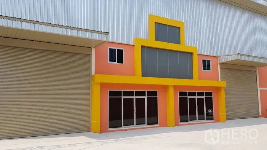 คลังสินค้า ให้เช่าในMueang Samut Prakan, Samut Prakan - ด้านหน้าโกดังพร้อมประตูม้วนขนาดใหญ่ สำนักงานกระจก และลานคอนกรีตกว้างสำหรับขนถ่ายสินค้า