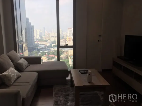 คอนโด ให้เช่าในKhlong Toei, Bangkok - มุมนั่งเล่นอบอุ่น โซฟารูปตัวแอล โต๊ะกลาง และหน้าต่างบานใหญ่ชมวิวเมือง