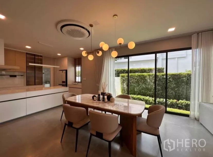 Detached House for rent in Samut Prakan - Dining area beside floor-to-ceiling windows overlooking a trimmed hedge garden.