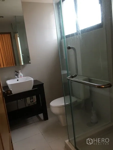 Condominium for rent in Pathum Wan, Bangkok - Modern bathroom with glass shower, white basin vanity, toilet and frosted window.
