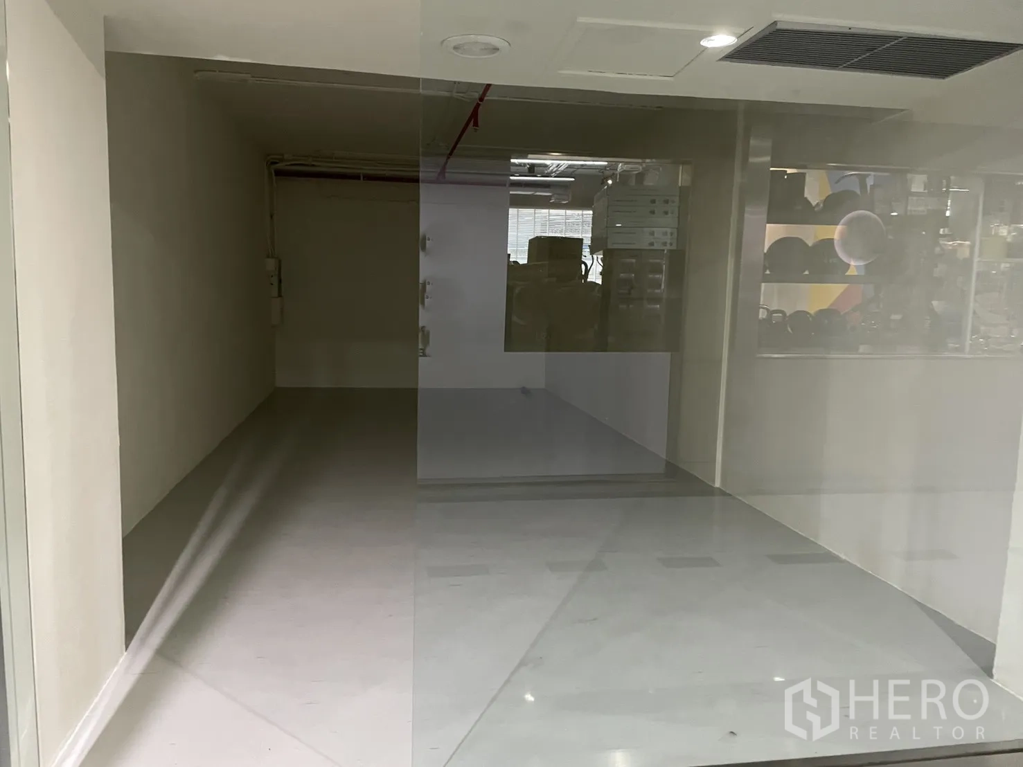 Retail Space for rent in Watthana, Bangkok - View through a full-height glass wall into the vacant shop with ceiling vent and lighting.