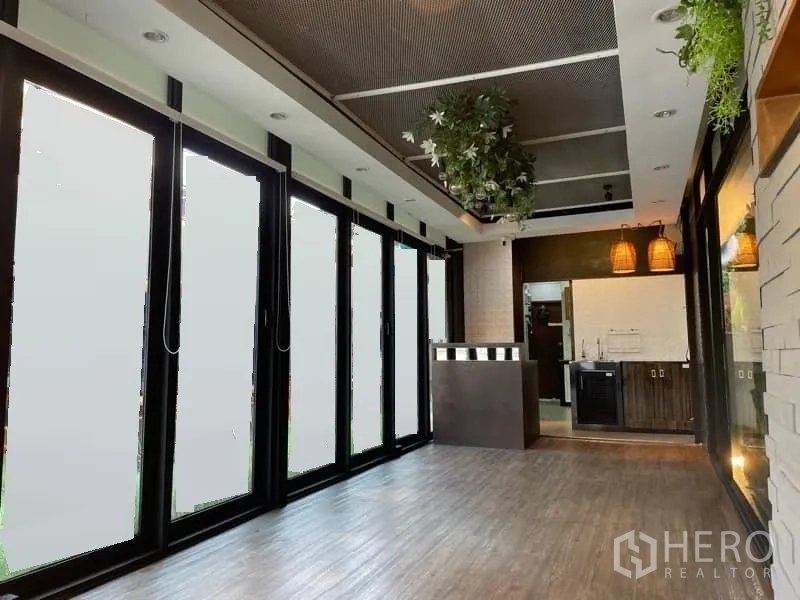 零售空间 出租在Watthana, Bangkok - 开放式铺面，整排可折叠落地玻璃、接待台、吊灯与木地板。