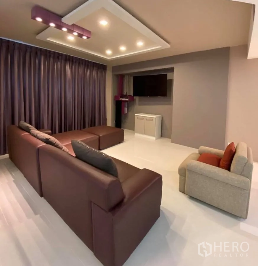 คอนโด ให้เช่าในWatthana, Bangkok - ห้องนั่งเล่นกว้างพร้อมโซฟาหนังสีน้ำตาล เก้าอี้เดี่ยว ไฟฝ้าซ่อน ผ้าม่านทึบ และผนังทีวี