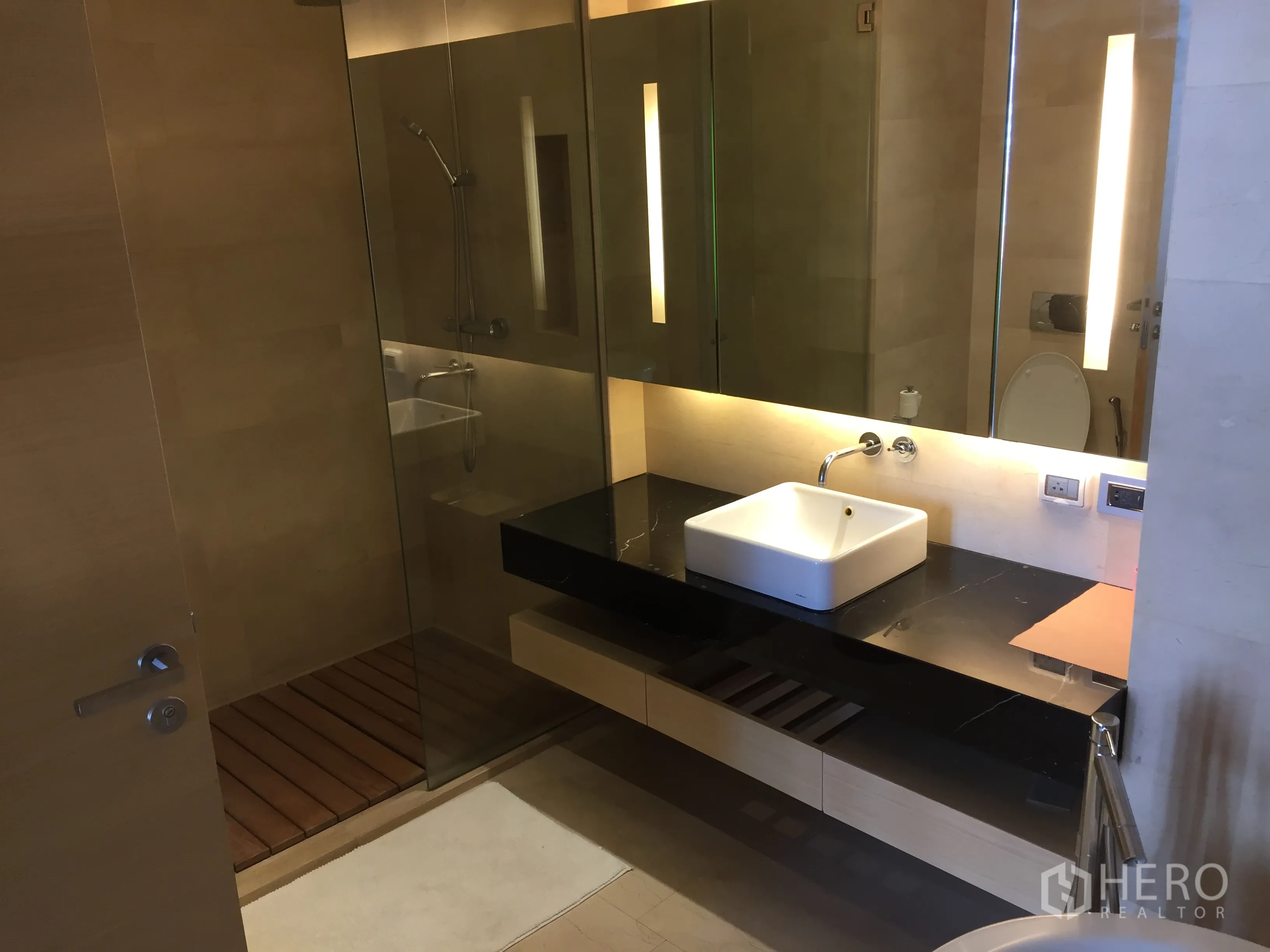 公寓 出租或出售在Bang Rak, Bangkok - 玻璃步入式淋浴间，长台面与灯带镜柜相邻。