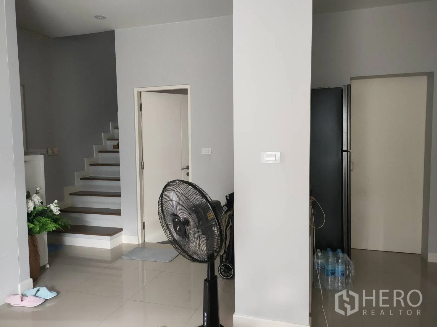 บ้าน ให้เช่าหรือขายในLam Luk Ka, Pathum Thani - โถงชั้นล่างเห็นบันได ประตูหลายบาน พื้นกระเบื้องเงา และพัดลมตั้งพื้น