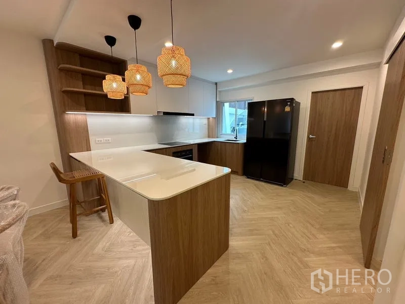 Home Office for rent in Khlong Toei, Bangkok - Modern L-shaped kitchen with white countertops, island breakfast bar and a black refrigerator.