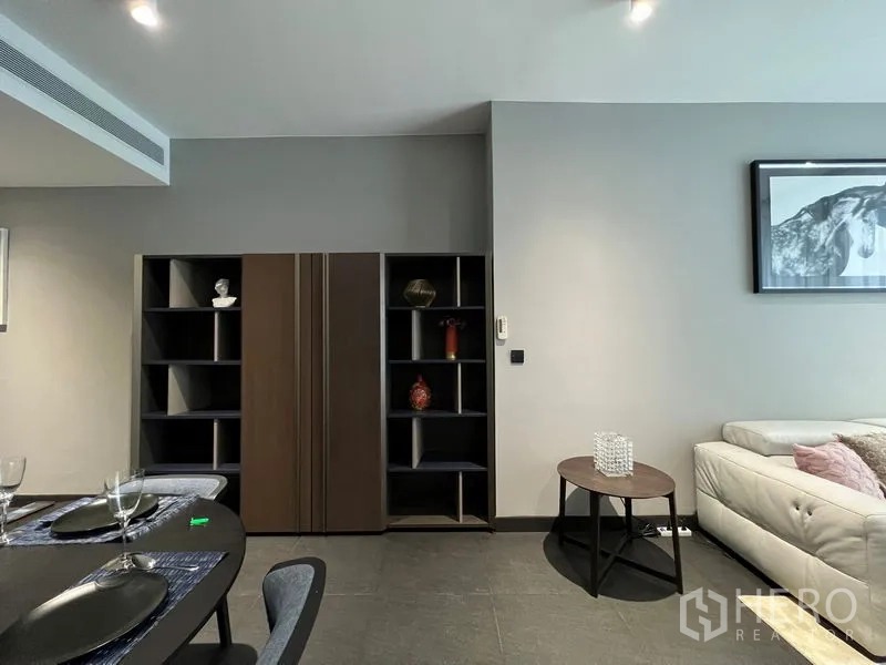 Condominium for rent in Bang Rak, Bangkok - Dining area beside open shelves and sofa in neutral tones.