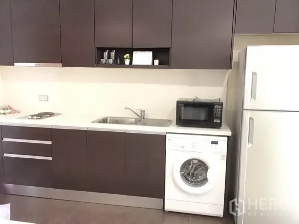 公寓 出租在Watthana, Bangkok - 现代一字型厨房，深色橱柜、洗槽、炉灶、微波炉、洗衣机及双门冰箱齐备。
