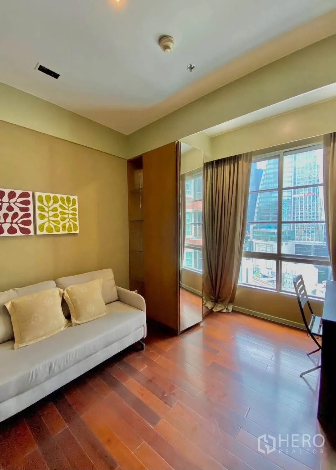 公寓 for rent in Khlong Toei, Bangkok - 明亮小房间配沙发与书桌，落地窗望向城市大楼。