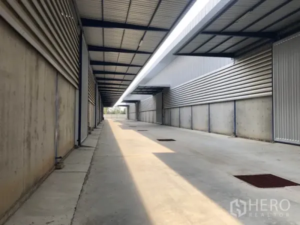 Warehouse for rent in Lat Lum Kaeo, Pathum Thani - Covered loading lane between warehouse units with metal roofing, concrete pavement and drainage grates.