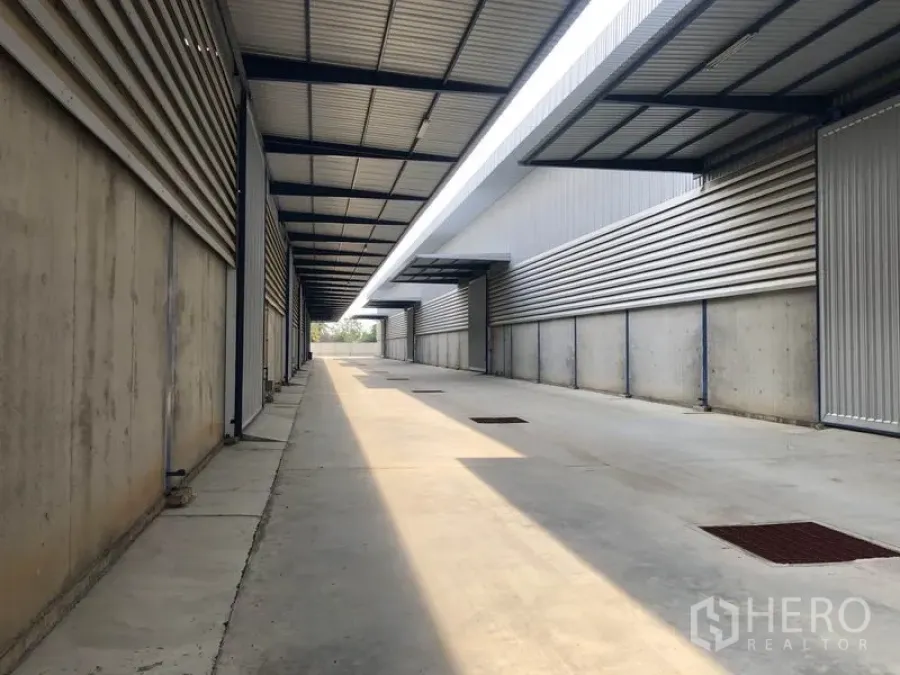 Warehouse for rent in Lat Lum Kaeo, Pathum Thani - Covered loading lane between warehouse units with metal roofing, concrete pavement and drainage grates.