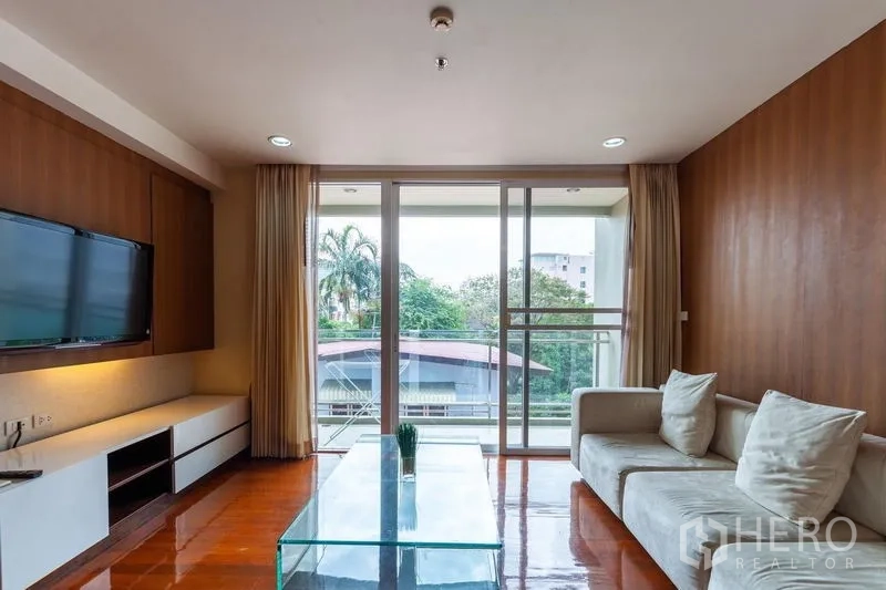 คอนโด ให้เช่าในWatthana, Bangkok - มุมนั่งเล่นโซฟารูปตัวแอล โต๊ะกลางกระจก และวิวสีเขียวจากระเบียง