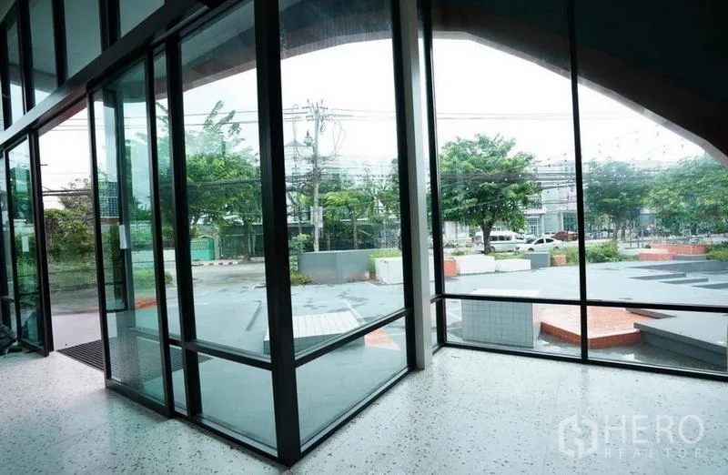 独立商业地产 出租在Bang Na, Bangkok - 室内玻璃转角望向前方停车区与绿树。